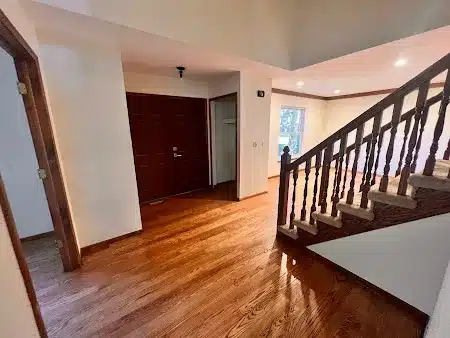 sunny entryway with hardwood floors, a dark wood front door, open closet, and a wooden staircase with railing. white walls and recessed lighting create a bright, welcoming atmosphere.