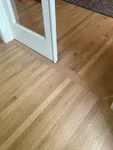 a door is open between two rooms with wooden floors. the flooring patterns in each room are noticeably misaligned where they meet under the door.