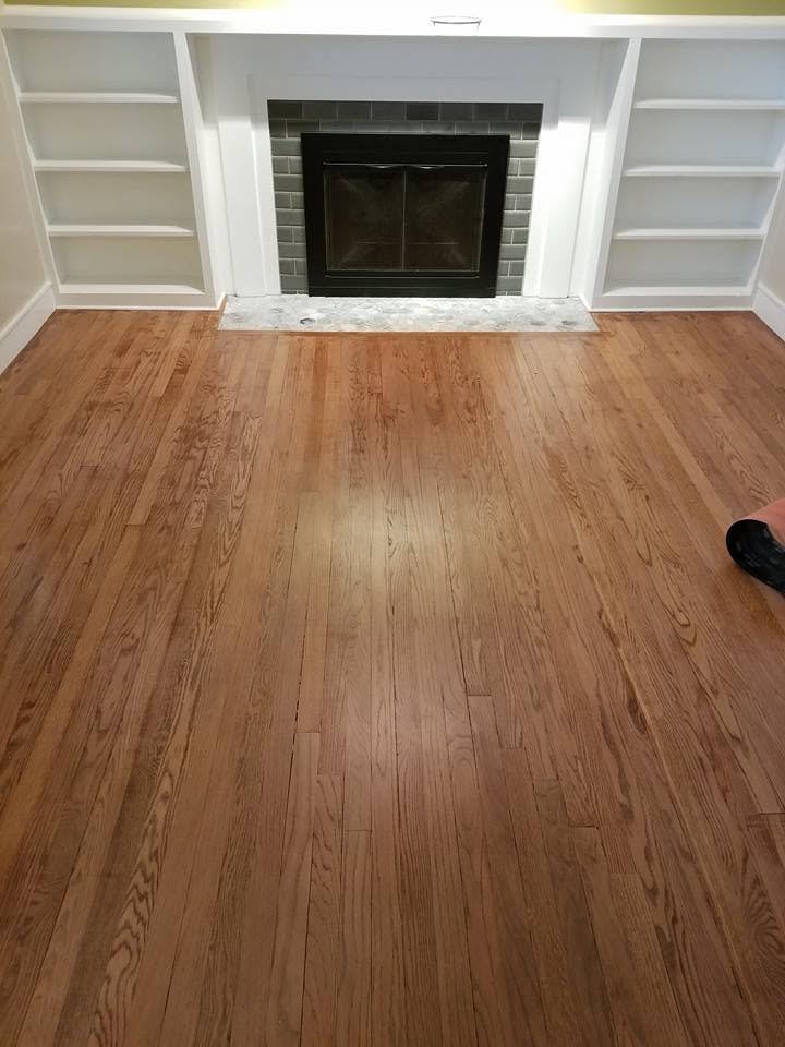 a wooden floor leads to a fireplace with a dark frame and gray tiles. white built in shelves are on either side. part of a person’s foot is visible on the right edge.